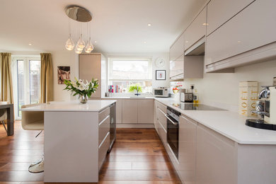 Inspiration for a medium sized contemporary l-shaped open plan kitchen in London with a built-in sink, flat-panel cabinets, beige cabinets, quartz worktops, white splashback, engineered quartz splashback, black appliances, dark hardwood flooring, an island, brown floors, white worktops and feature lighting.