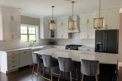 Example of a large mountain style l-shaped dark wood floor and brown floor eat-in kitchen design in Other with a farmhouse sink, shaker cabinets, white cabinets, quartz countertops, white backsplash, ceramic backsplash, black appliances, an island and white countertops