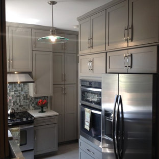 Cette image montre une petite arrière-cuisine traditionnelle en U avec aucun îlot, un placard avec porte à panneau surélevé, des portes de placard beiges, un plan de travail en verre recyclé, une crédence grise, une crédence en carreau de verre, un électroménager en acier inoxydable, un évier de ferme et un sol en carrelage de porcelaine.