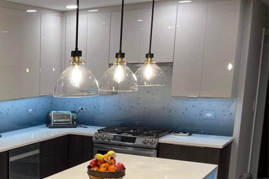Example of a trendy kitchen design in Detroit with flat-panel cabinets, blue backsplash, glass sheet backsplash and white countertops