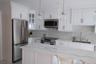 This is an example of a mid-sized transitional l-shaped kitchen in Toronto with an undermount sink, raised-panel cabinets, white cabinets, stainless steel appliances and with island.