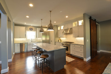 Large transitional l-shaped dark wood floor and brown floor eat-in kitchen photo in St Louis with a farmhouse sink, shaker cabinets, white cabinets, granite countertops, white backsplash, subway tile backsplash, stainless steel appliances, an island and gray countertops