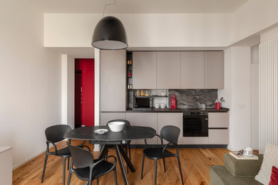 Idee per una cucina design con ante lisce, ante grigie, paraspruzzi nero, paraspruzzi in lastra di pietra, elettrodomestici neri, pavimento in legno massello medio, nessuna isola, pavimento marrone e top nero