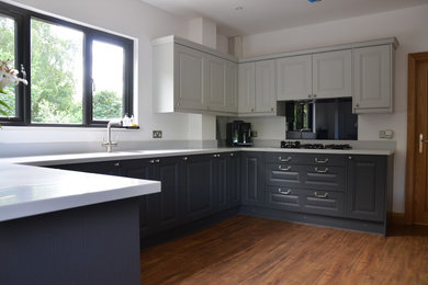 This is an example of a medium sized traditional u-shaped enclosed kitchen in Essex with a breakfast bar, a submerged sink, shaker cabinets, grey cabinets, composite countertops, white splashback, laminate floors and brown floors.