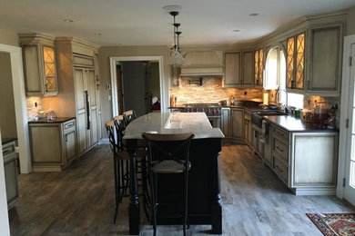Example of a mid-sized mountain style l-shaped ceramic tile eat-in kitchen design in New York with a farmhouse sink, recessed-panel cabinets, granite countertops, stone tile backsplash, stainless steel appliances and an island