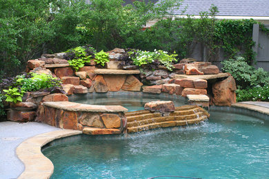 This is an example of a large transitional backyard custom-shaped pool in Dallas with natural stone pavers and a hot tub.