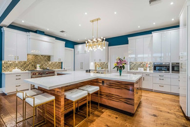 Inspiration for a large contemporary l-shaped medium tone wood floor and brown floor open concept kitchen remodel in Tampa with flat-panel cabinets, white cabinets, quartz countertops, metallic backsplash, porcelain backsplash, stainless steel appliances, an island, white countertops and an undermount sink