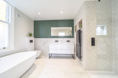 Inspiration for a medium sized contemporary ensuite bathroom in London with flat-panel cabinets, white cabinets, a freestanding bath, a walk-in shower, a wall mounted toilet, grey tiles, porcelain tiles, green walls, porcelain flooring, a console sink, grey floors, an open shower, double sinks and a freestanding vanity unit.