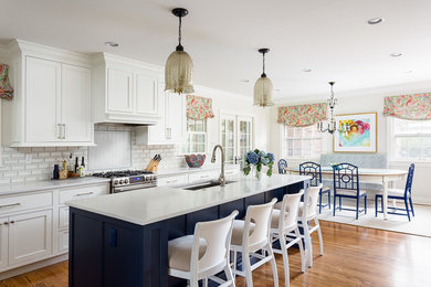 This is an example of a mid-sized beach style eat-in kitchen in Louisville with a single-bowl sink, white cabinets, quartz benchtops, white splashback, ceramic splashback, stainless steel appliances, with island, brown floor, white benchtop, medium hardwood floors and beaded inset cabinets.