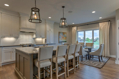 Eat-in kitchen - mid-sized transitional l-shaped medium tone wood floor and beige floor eat-in kitchen idea in Omaha with an undermount sink, recessed-panel cabinets, white cabinets, granite countertops, white backsplash, subway tile backsplash, stainless steel appliances and an island