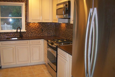 Photo of a mid-sized traditional u-shaped open plan kitchen in Baltimore with an undermount sink, raised-panel cabinets, white cabinets, solid surface benchtops, brown splashback, glass tile splashback, stainless steel appliances, ceramic floors and a peninsula.