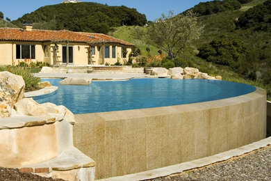 Inspiration for an expansive mediterranean backyard custom-shaped infinity pool in Santa Barbara with natural stone pavers and a hot tub.