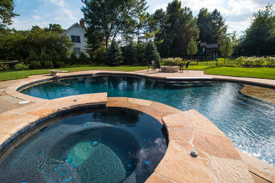 Mid-sized traditional backyard custom-shaped natural pool in Chicago with a hot tub and natural stone pavers.