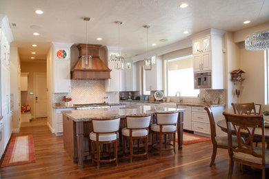Example of a large transitional dark wood floor and brown floor eat-in kitchen design in Salt Lake City with a farmhouse sink, raised-panel cabinets, white cabinets, granite countertops, beige backsplash, porcelain backsplash, stainless steel appliances, an island and beige countertops