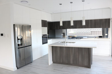 Photo of a large modern l-shaped open plan kitchen in Sydney with a double-bowl sink, flat-panel cabinets, white cabinets, quartz benchtops, grey splashback, glass sheet splashback, stainless steel appliances, multiple islands and white benchtop.