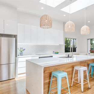 Photo of a large contemporary galley kitchen pantry in Gold Coast - Tweed with an undermount sink, flat-panel cabinets, white cabinets, quartzite benchtops, white splashback, ceramic splashback, coloured appliances, medium hardwood floors, with island and brown floor.