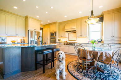 Example of a large classic l-shaped brown floor and medium tone wood floor eat-in kitchen design in Denver with a farmhouse sink, recessed-panel cabinets, granite countertops, porcelain backsplash, stainless steel appliances, an island, beige cabinets and beige backsplash