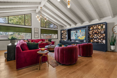 Inspiration for a large eclectic open concept medium tone wood floor, brown floor and vaulted ceiling living room remodel in Orange County with white walls, no fireplace and a media wall