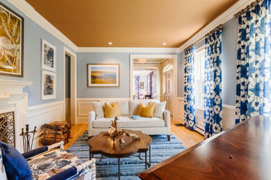 This is an example of a mid-sized transitional living room in Boston with a music area, blue walls, light hardwood floors, a standard fireplace, a wood fireplace surround, beige floor, recessed and wallpaper.