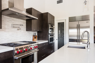 Inspiration for a mid-sized u-shaped medium tone wood floor kitchen remodel in Orange County with a single-bowl sink, flat-panel cabinets, brown cabinets, quartz countertops, multicolored backsplash, stone tile backsplash, stainless steel appliances, an island and white countertops