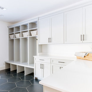 Modelo de lavadero multiusos, actual, extra grande, con fregadero sobremueble, armarios estilo shaker, puertas de armario grises, encimera de cuarzo compacto, paredes blancas, suelo de baldosas de cerámica, lavadora y secadora juntas, suelo negro y encimeras blancas