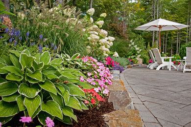 This is an example of a large coastal full sun backyard concrete paver landscaping in Portland Maine for summer.