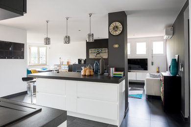 This is an example of a large modern galley open plan kitchen in Other with a single-bowl sink, tile benchtops, black splashback, ceramic splashback, panelled appliances, ceramic floors, with island, black floor and black benchtop.