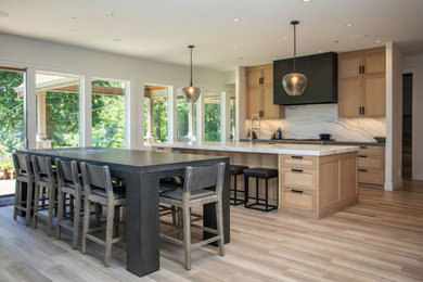 Large trendy l-shaped light wood floor kitchen photo in Portland with shaker cabinets, light wood cabinets, solid surface countertops, white backsplash, stone slab backsplash, stainless steel appliances, an island and white countertops
