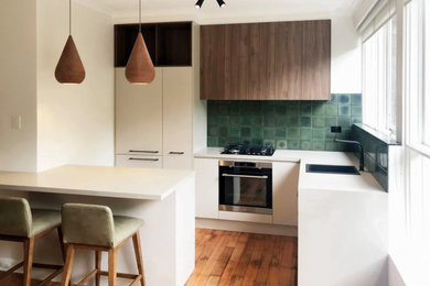 Photo of a mid-sized modern u-shaped separate kitchen in Melbourne with flat-panel cabinets, white cabinets, quartz benchtops, green splashback, light hardwood floors and no island.