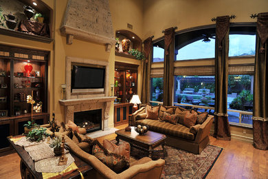 Inspiration for a large mediterranean open concept medium tone wood floor and brown floor family room remodel in Other with beige walls, a standard fireplace, a wall-mounted tv and a stone fireplace