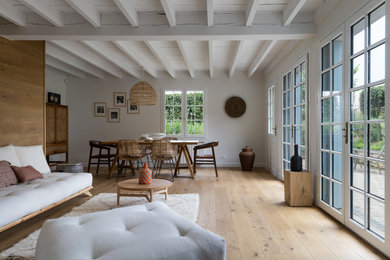 Idée de décoration pour une très grande salle de séjour bohème ouverte avec un mur blanc, parquet clair, aucun téléviseur, un sol beige et poutres apparentes.