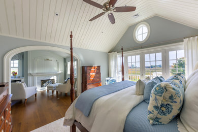 ボストンにある中くらいなビーチスタイルのおしゃれな主寝室 (青い壁、濃色無垢フローリング、標準型暖炉、木材の暖炉まわり、茶色い床、三角天井)