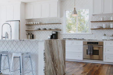 Open concept kitchen - large farmhouse l-shaped medium tone wood floor and brown floor open concept kitchen idea in Other with an undermount sink, shaker cabinets, white cabinets, marble countertops, white backsplash, porcelain backsplash, stainless steel appliances, an island and brown countertops