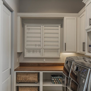 デトロイトの巨大なラスティックスタイルのおしゃれなランドリールーム (アンダーカウンターシンク、レイズドパネル扉のキャビネット、中間色木目調キャビネット、クオーツストーンカウンター、スレートの床、緑の床、ベージュの壁、左右配置の洗濯機・乾燥機) の写真