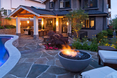 Large elegant backyard stone patio photo in Vancouver with a fire pit and a roof extension