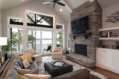 Large transitional open concept medium tone wood floor and brown floor living room photo in Charlotte with gray walls, a standard fireplace, a stone fireplace and a wall-mounted tv