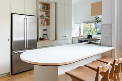 Contemporary u-shaped eat-in kitchen in Melbourne with a double-bowl sink, flat-panel cabinets, beige cabinets, solid surface benchtops, beige splashback, ceramic splashback, stainless steel appliances, medium hardwood floors, with island, brown floor and white benchtop.