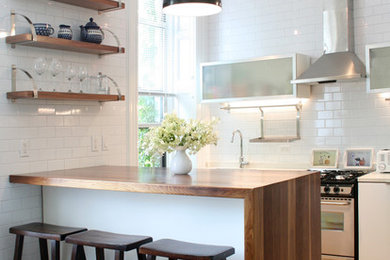 Eat-in kitchen - mid-sized modern l-shaped light wood floor eat-in kitchen idea in New York with an undermount sink, flat-panel cabinets, wood countertops, white backsplash, ceramic backsplash, stainless steel appliances, an island and white cabinets