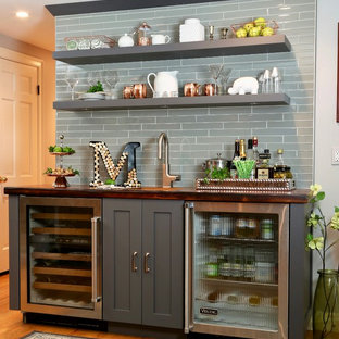 他の地域の中サイズのトランジショナルスタイルのおしゃれなウェットバー (アンダーカウンターシンク、グレーのキャビネット、木材カウンター、グレーのキッチンパネル、ガラスタイルのキッチンパネル、無垢フローリング、茶色いキッチンカウンター、シェーカースタイル扉のキャビネット) の写真