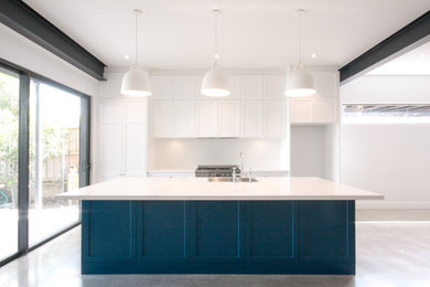 This is an example of a modern open plan kitchen in Sydney with a drop-in sink, recessed-panel cabinets, blue cabinets, solid surface benchtops, white splashback, ceramic splashback, stainless steel appliances, concrete floors, with island, grey floor, white benchtop and exposed beam.