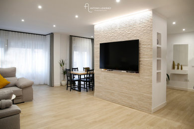 Diseño de salón abierto y beige y blanco moderno grande de obra sin chimenea con paredes blancas, suelo de madera clara, televisor colgado en la pared, suelo beige y piedra