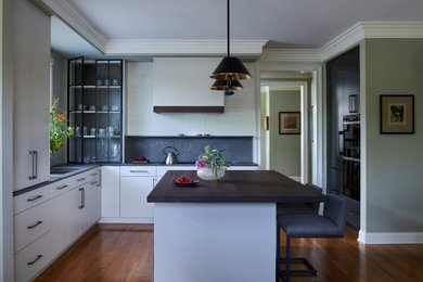 Idées déco pour une cuisine moderne de taille moyenne avec îlot, un évier 1 bac, un placard à porte plane, des portes de placard blanches, une crédence grise, un électroménager noir, un sol en bois brun, un sol marron et un plan de travail gris.