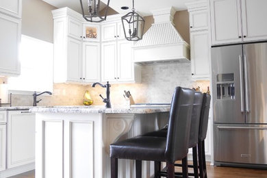 Example of a large transitional l-shaped medium tone wood floor kitchen design in New York with recessed-panel cabinets, white cabinets, granite countertops, gray backsplash, subway tile backsplash, stainless steel appliances, an island and a farmhouse sink