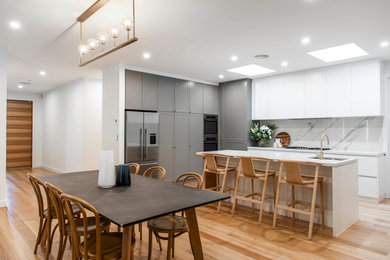 Contemporary l-shaped kitchen in Canberra - Queanbeyan with an undermount sink, yellow cabinets, quartz benchtops, white splashback, stone slab splashback, light hardwood floors and with island.