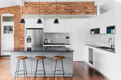 Contemporary l-shaped kitchen in Sydney with an undermount sink, flat-panel cabinets, white cabinets, grey splashback, stainless steel appliances, medium hardwood floors, with island and brown floor.