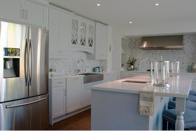 Open concept kitchen - mid-sized transitional l-shaped medium tone wood floor open concept kitchen idea in Toronto with a farmhouse sink, recessed-panel cabinets, blue cabinets, quartz countertops, multicolored backsplash, mosaic tile backsplash, stainless steel appliances and an island