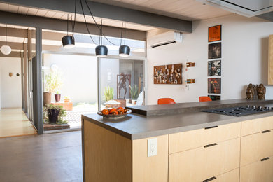 Mid-sized mid-century modern galley concrete floor, gray floor and exposed beam eat-in kitchen photo in Orange County with flat-panel cabinets, light wood cabinets, solid surface countertops, a peninsula and gray countertops
