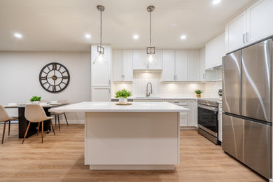 Mid-sized l-shaped vinyl floor and brown floor eat-in kitchen photo in Vancouver with an undermount sink, shaker cabinets, white cabinets, quartz countertops, white backsplash, subway tile backsplash, stainless steel appliances, an island and white countertops