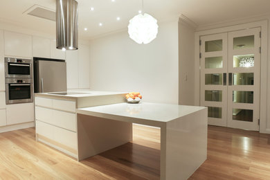 This is an example of a mid-sized modern l-shaped open plan kitchen in Melbourne with an undermount sink, flat-panel cabinets, white cabinets, quartz benchtops, stainless steel appliances, light hardwood floors and with island.