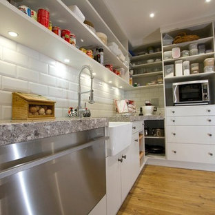 Farmhouse kitchen pantry designs - Cottage medium tone wood floor kitchen pantry photo in Napier-Hastings with a farmhouse sink, quartz countertops, white backsplash, stainless steel appliances and two islands